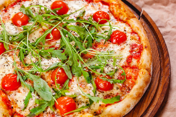 Italian Pizza with tomatoes, mozzarella cheese and arugula on wooden cutting board. Close up - Photo, Image