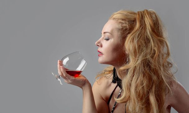 Attractive middle age woman with snifter of brandy. Beautiful forty years blonde with long hair on a white background. - Φωτογραφία, εικόνα