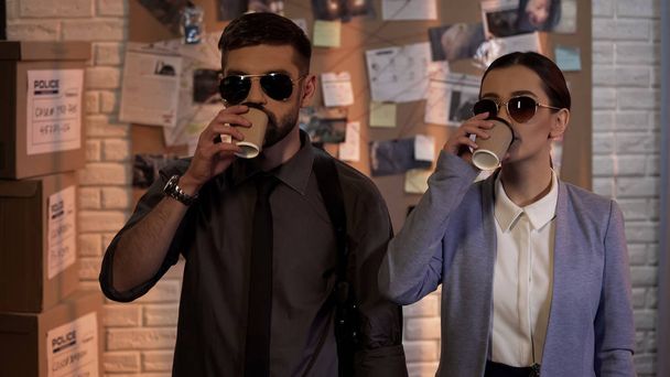 Cool professional detectives in eyeglasses drinking coffee, private agency - Foto, Imagen