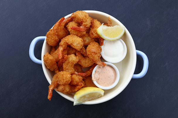 Close up portion of battered and breaded shrimps with dipping sauces served in cooking pot over blue table copy space, elevated top view, directly above - Фото, изображение
