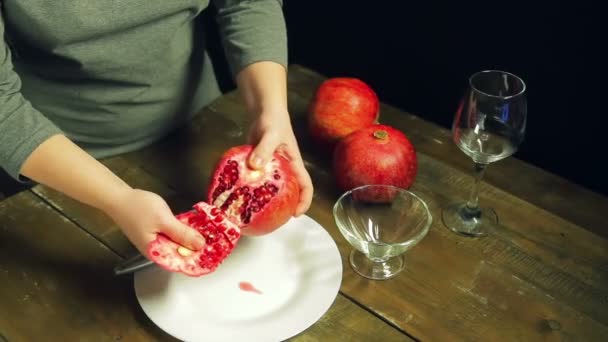 Woman cleans pomegranate fruit on a white plate on a wooden table - Felvétel, videó