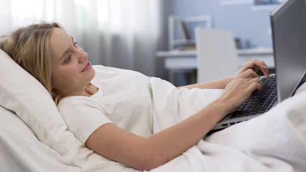 Adolescente acostada en la cama con el ordenador portátil, problema de adicción a las redes sociales
 - Foto, Imagen
