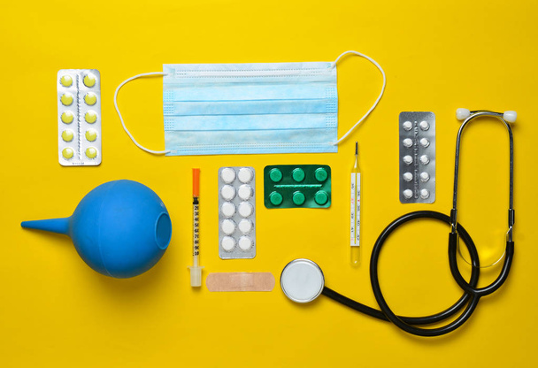 Medische apparatuur op een gele achtergrond. Klysma, blaren pillen, notebook, stethoscoop, spuit, thermometer. Medische concept, bovenaanzicht, plat lag styl - Foto, afbeelding