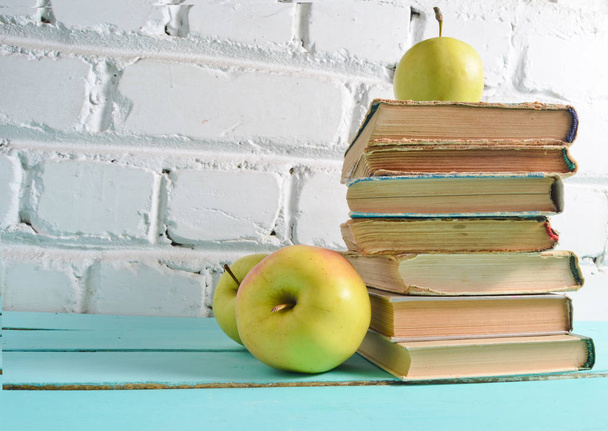 Pilha de livros antigos, maçã em um fundo de parede de tijolo branco. Conceito escolar, educação
 - Foto, Imagem