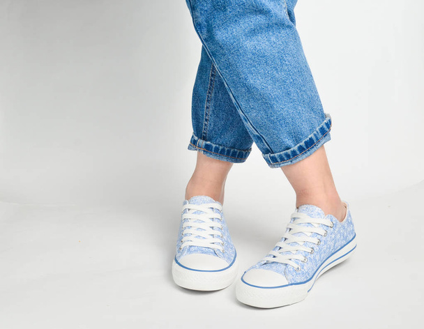 Frauenbeine in kurzen Jeans und Turnschuhen stehen auf weißem Untergrund - Foto, Bild