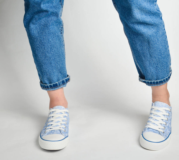 Female legs in short jeans and sneakers stand on a white backgroun - Foto, Imagen