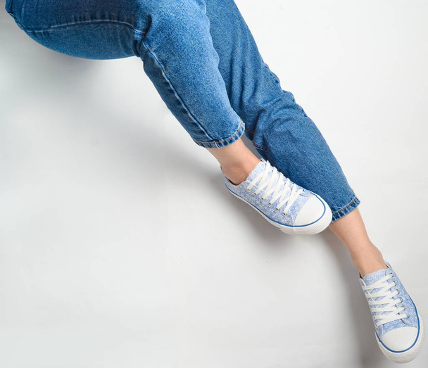 Female legs in jeans and sneakers on a white background. Top Vie - Фото, изображение