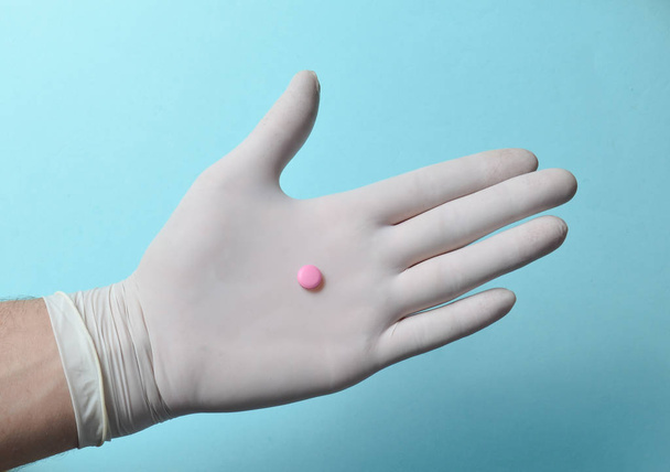 Pink tablet on medic hand with white latex gloves on a blue background. Medical concep - Photo, Image