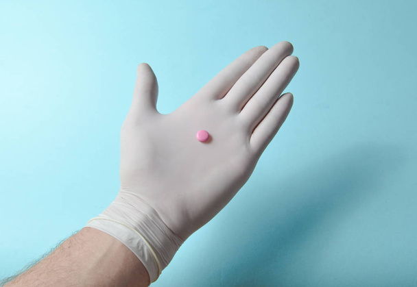 Comprimido rosa na mão médica com luvas de látex branco sobre um fundo azul. Conceito médico
 - Foto, Imagem