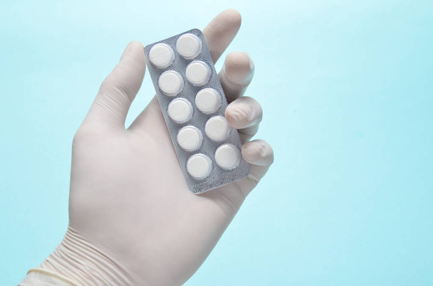Рука медика в белых латексных перчатках держит волдырь с таблетками на синем фоне. Медицинская концепция
 - Фото, изображение