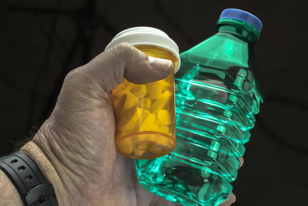 Man holds with left hand a bottle of water and a pill bottle - Photo, Image