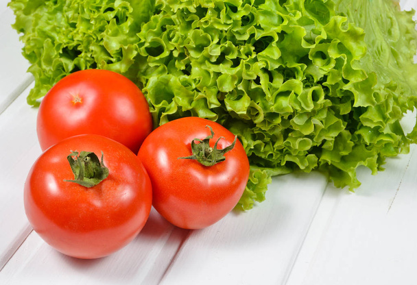 Листя зеленого салату, стиглі червоні помідори на білому дерев'яному табуреті
 - Фото, зображення