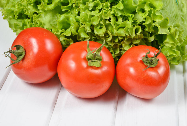 Green lettuce leaves, ripe red tomatoes on a white wooden tabl - Photo, Image
