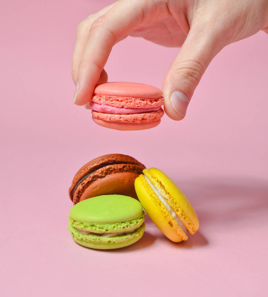 Female hand lowers the pink macaroons cookies. Many macaroons on a pink pastel background. Minimalis - Photo, Image