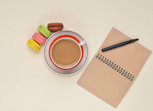 Tasse Kaffee, farbige Makronen, Notizblock mit Stift auf weißem Hintergrund - Foto, Bild