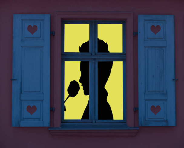 lighted window frame with a silhouette of a romantic person smelling a rose, valentines day concept - Foto, immagini