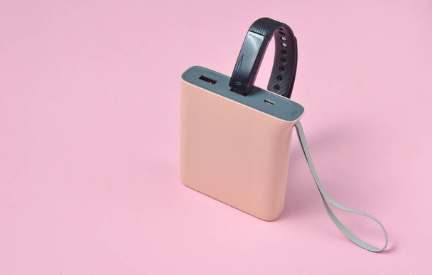 Power bank charged  smart bracelet on a pink pastel background. Modern gadgets - Photo, Image