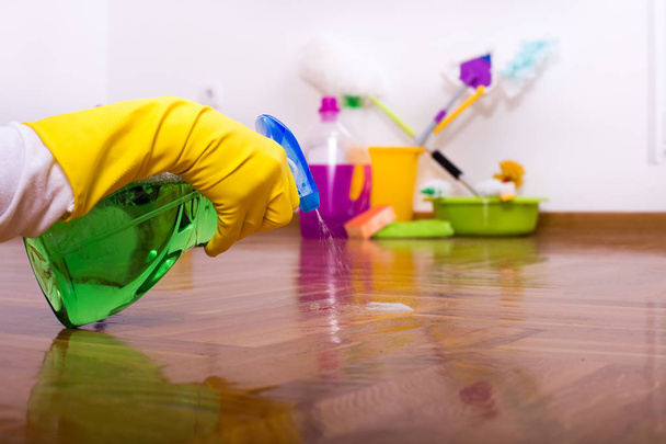 Close up de mão do dono da casa espirrando detergente com frasco de spray em parquet com equipamento de limpeza no chão no fundo
 - Foto, Imagem