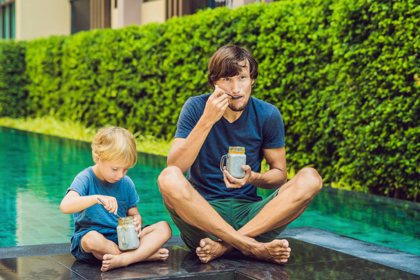 Father and son eat dessert with chia seeds and mangoes by the pool in the morning. healthy eating, vegetarian food, diet and people concept - Photo, Image