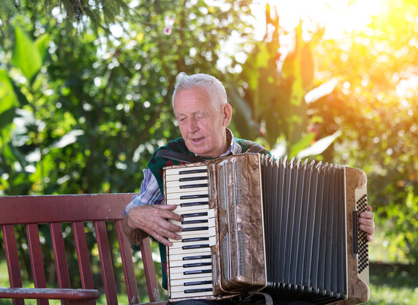 高齢男性の庭のベンチにアコーディオンを演奏 - 写真・画像