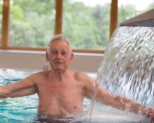 Літній чоловік насолоджується в басейні з гарячою водою і масажним душем у курортному комплексі
 - Фото, зображення