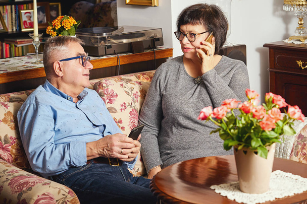 šťastní senioři pár sedí na gauči, zatímco žena mluvila po telefonu. - Fotografie, Obrázek