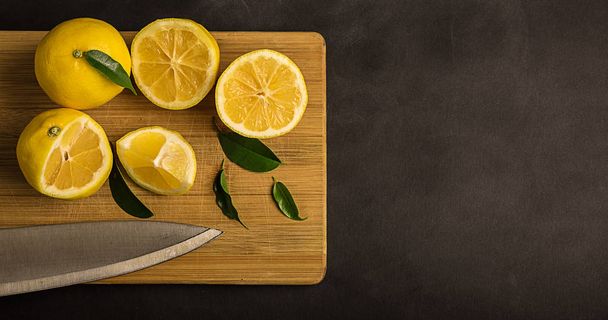 Yellow lemons and leaves on a cutting board - Zdjęcie, obraz