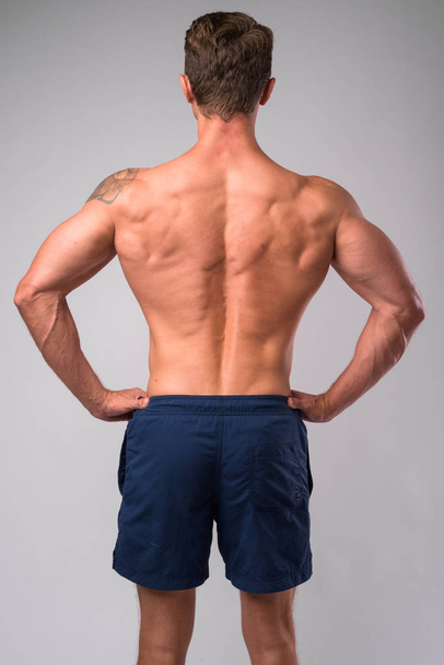 Vista posteriore dell'uomo muscoloso senza maglietta con le mani sui fianchi
 - Foto, immagini