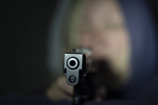 Una mujer sostiene un arma en su mano y la apunta a la cámara. Concéntrate en la parte delantera del arma.
. - Foto, imagen