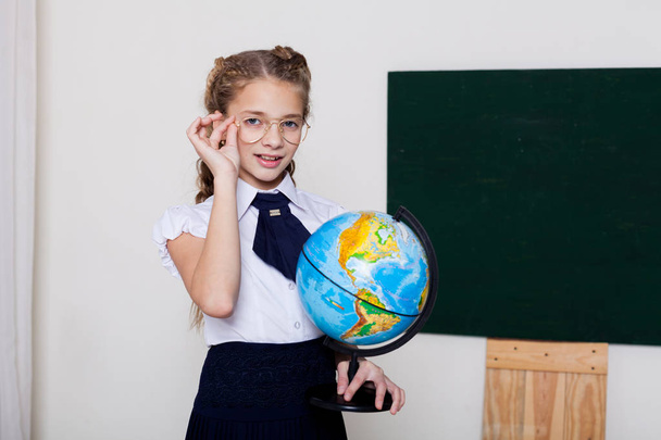 κορίτσι σχολείο κορίτσι στέκεται στο μαυροπίνακα με σφαίρα - Φωτογραφία, εικόνα