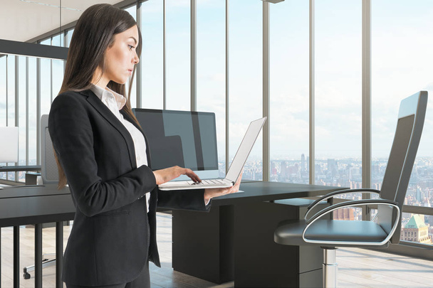 Красива бізнес-леді, використовуючи ноутбук в сучасному офісі з панорамним видом на місто. Технологія та концепція комунікації
. - Фото, зображення