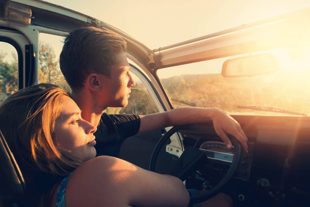 Happy young couple in a car enjoying the beautiful sunset in countryside. - Photo, Image