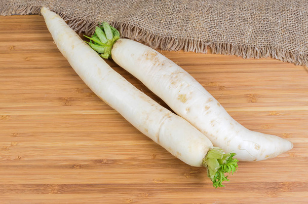 Top view of two fresh washed daikon radish with torn off haulm on a wooden bamboo surface with sackcloth - Photo, Image