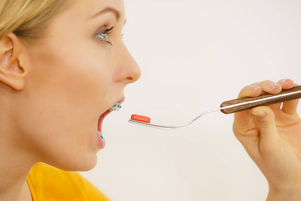 Young woman taking pill, eating one medicine on fork. Healthcare and medical condition concept. - Photo, Image