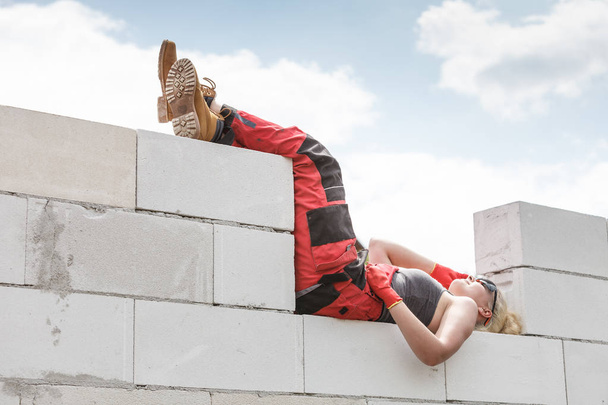 Blonde woman wearing dungarees relaxing after hard work on construction site. Female taking break dreaming of building her home. - Foto, immagini