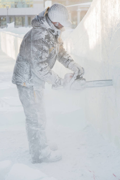 Ο γλύπτης κόβει περιγράμματα πάγο από τον πάγο με ένα αλυσοπρίονο για τα Χριστούγεννα - Φωτογραφία, εικόνα
