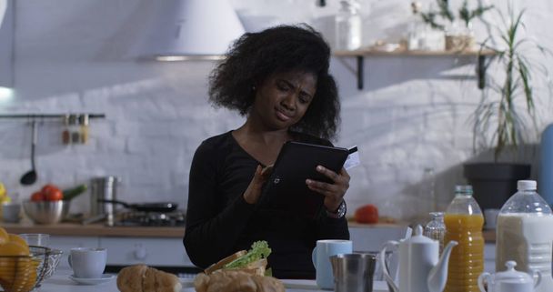 Woman using her tablet in the kitchen - Foto, afbeelding