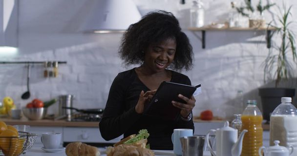 Woman using her tablet in the kitchen - Foto, afbeelding
