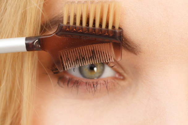 Close up of woman doing her make up, preparing lashes using brush tool brushing eyelashes. - Foto, afbeelding