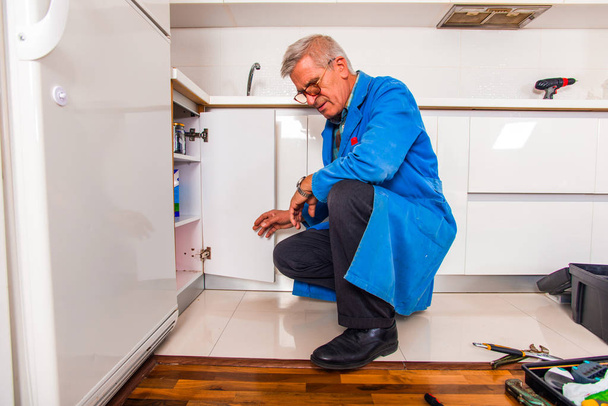 Σοβαρή πολυτεχνίτης στέκεται στην κουζίνα και για τον καθορισμό το ντουλάπι - Φωτογραφία, εικόνα