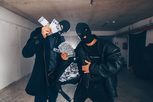 Des criminels se tiennent dans un garage sombre et montrent un sac plein d'argent volé
 - Photo, image