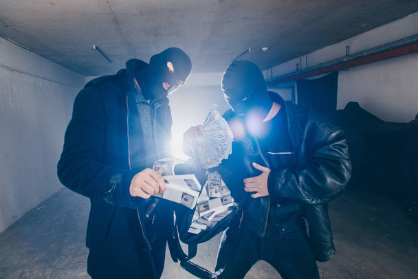 Масковані грабіжники стоять у темному коридорі, тримаючи мішок повний грошей
 - Фото, зображення