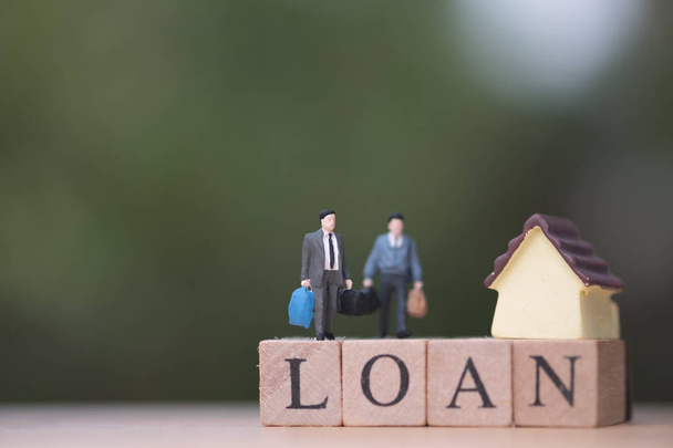 Miniature people businessman standing with wood word LOAN and blurred green nature as background. Trading house concept - 写真・画像