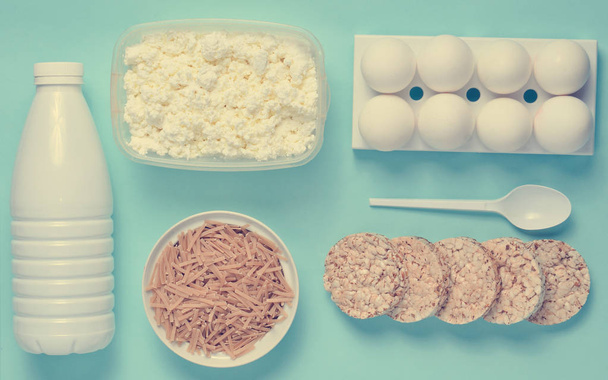 Dieet, gezonde voeding. Fles van yoghurt, knapperige ronde boekweitnoedels, cottage kaas, brood, ei lade op een blauwe achtergrond. Het concept van het verliezen van gewicht. Plat lag, top vie - Foto, afbeelding