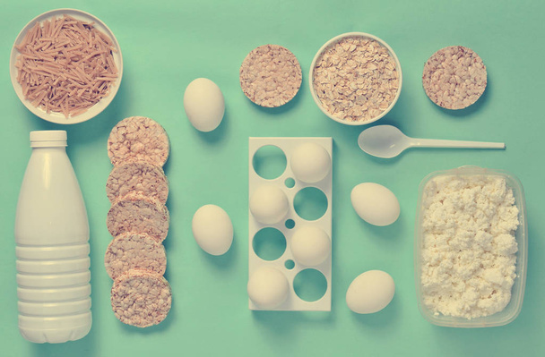 Diet, healthy food. Bottle of yogurt, crispy round bread, buckwheat noodles, oatmeal, cottage cheese, egg tray on a blue background. The concept of losing weight. flat lay, top vie - Photo, Image