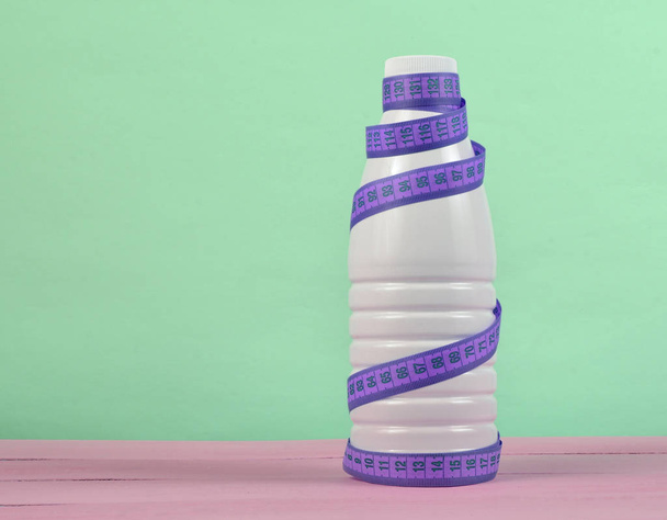 Botella de yogur envuelta en una regla sobre un fondo rosa, dietético, adelgazante cóncavo
 - Foto, Imagen