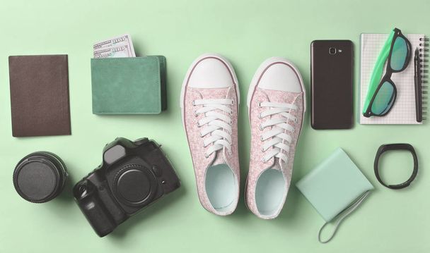 Gadgetek és tartozékok elrendezés a pasztell rózsaszín háttér. Cipők, fényképészeti eszközök, erszényes dollárt, intelligens óra, okostelefon, notebook, napszemüveg. Fogalmának utazás, tárgyak, top vie - Fotó, kép
