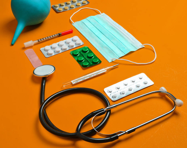 Medical equipment on a yellow background. Enema, blisters pills, notepad, stethoscope, syringe, thermometer. Medical concep - Photo, Image