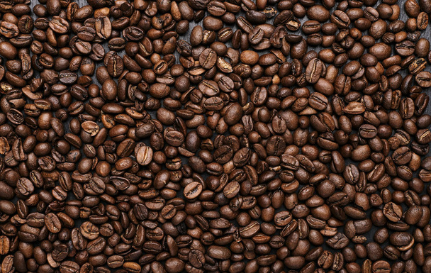 top view of roasted aromatic coffee beans on black wooden table - Photo, Image