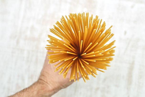 cropped image of man holding bunch of raw spaghetti in glass over wooden table  - Foto, afbeelding